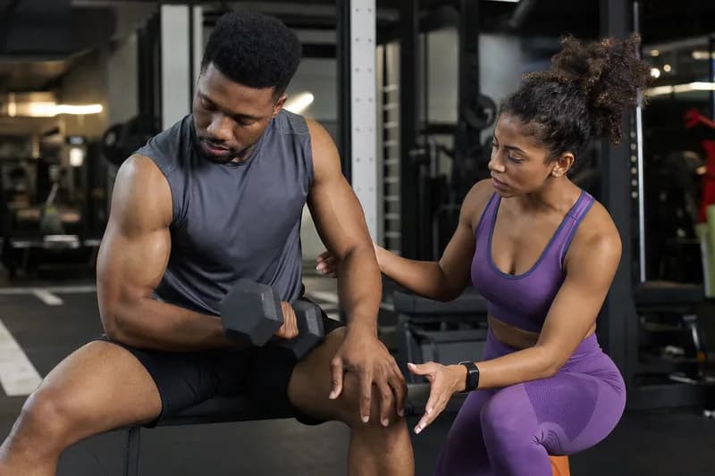 Personal trainer orientando aluno com halteres em academia